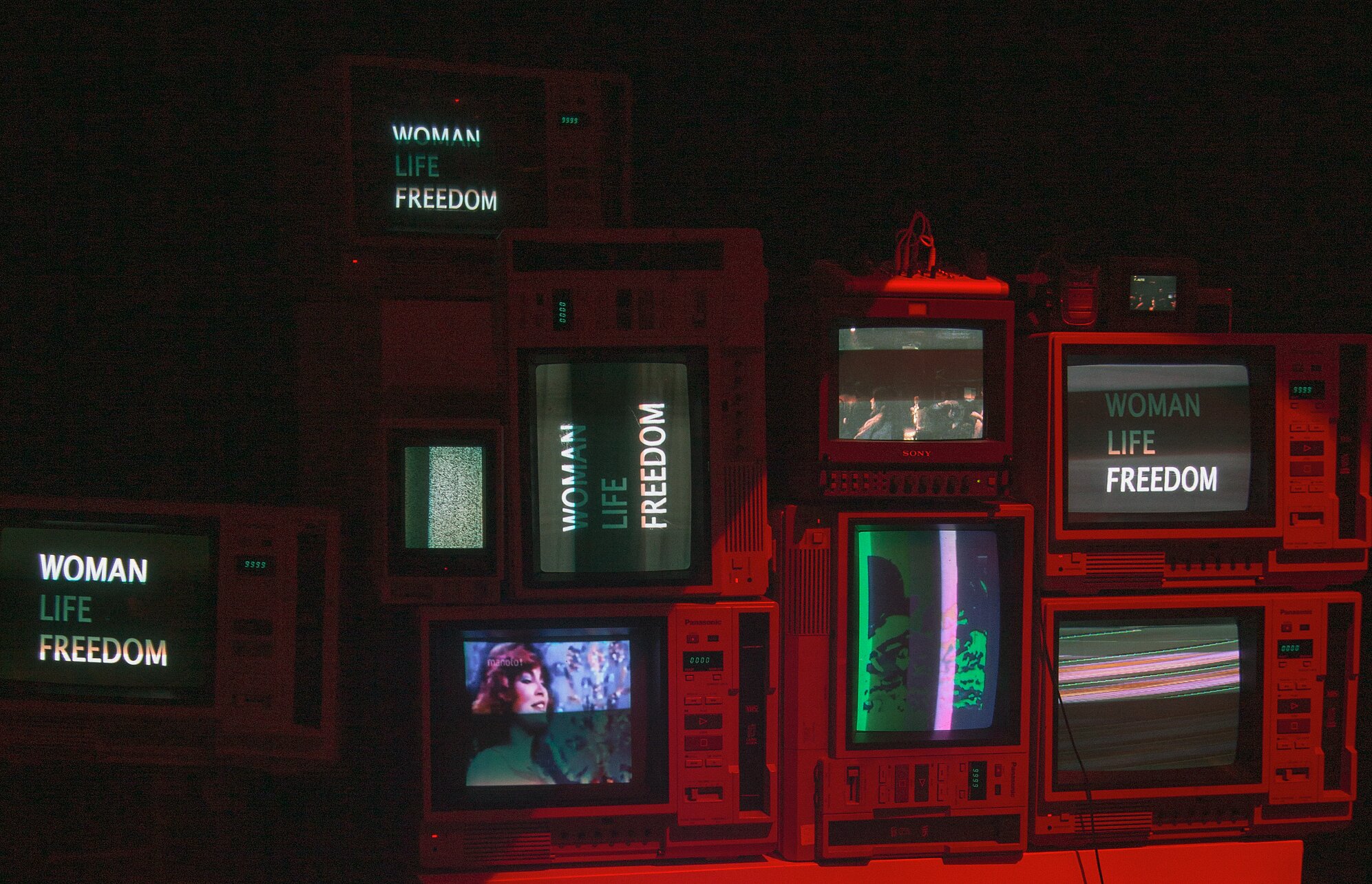 An art installation comprised of old television monitors displaying the words "WOMAN, LIFE, FREEDOM" and images from 1970s Iran.