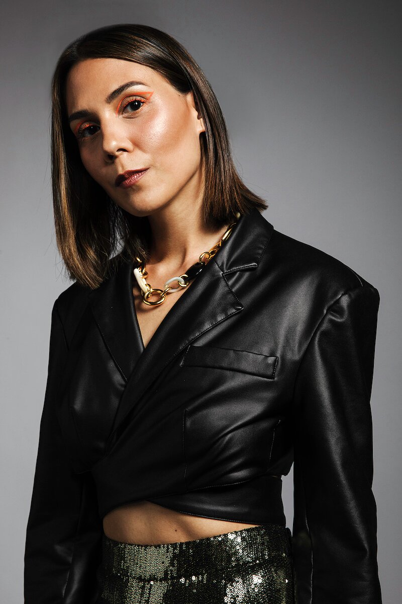 A photograph of the musician Sirintip dressed in a faux leather shirt and wearing orange graphic eyeliner.