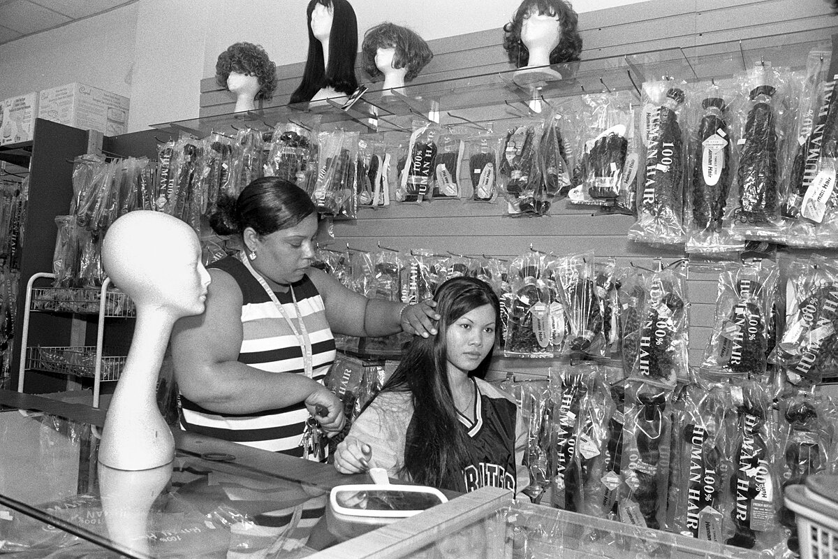 A woman brushes another woman's hair behind the counter of a beauty supply shop.