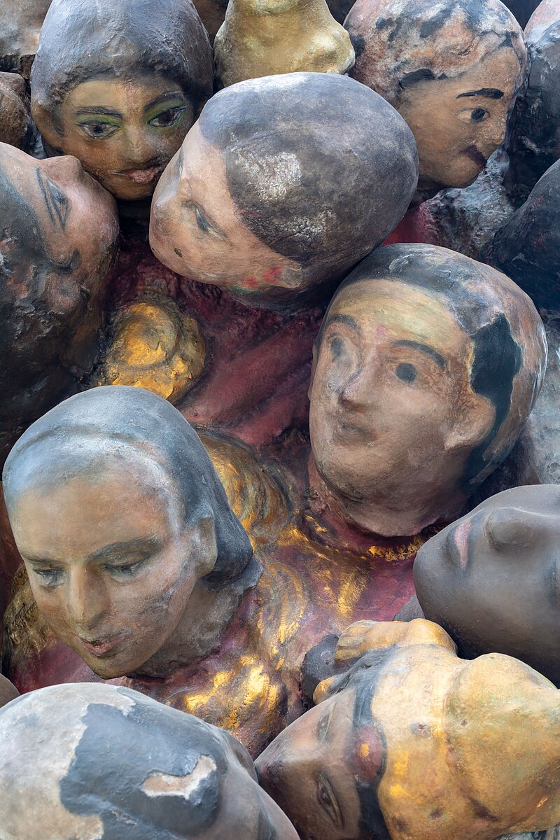 A close-up of dozens of small painted bronze heads.