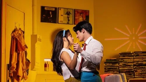 two performers waltz inside a yellow room featuring stacks of vinyl records