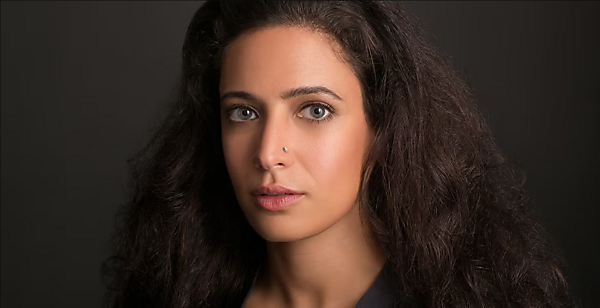 An Arab woman looks sternly at the camera against a plain background