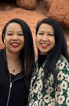 Two artists smile at the camera. They both have long black hair.