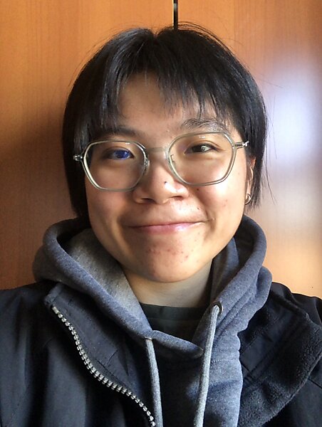 An Asian face with clear glasses and short hair posing against a wood wall.
