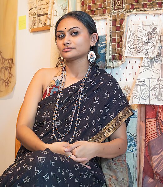 An Asian woman smiles against a backdrop with artwork pinned to the wall