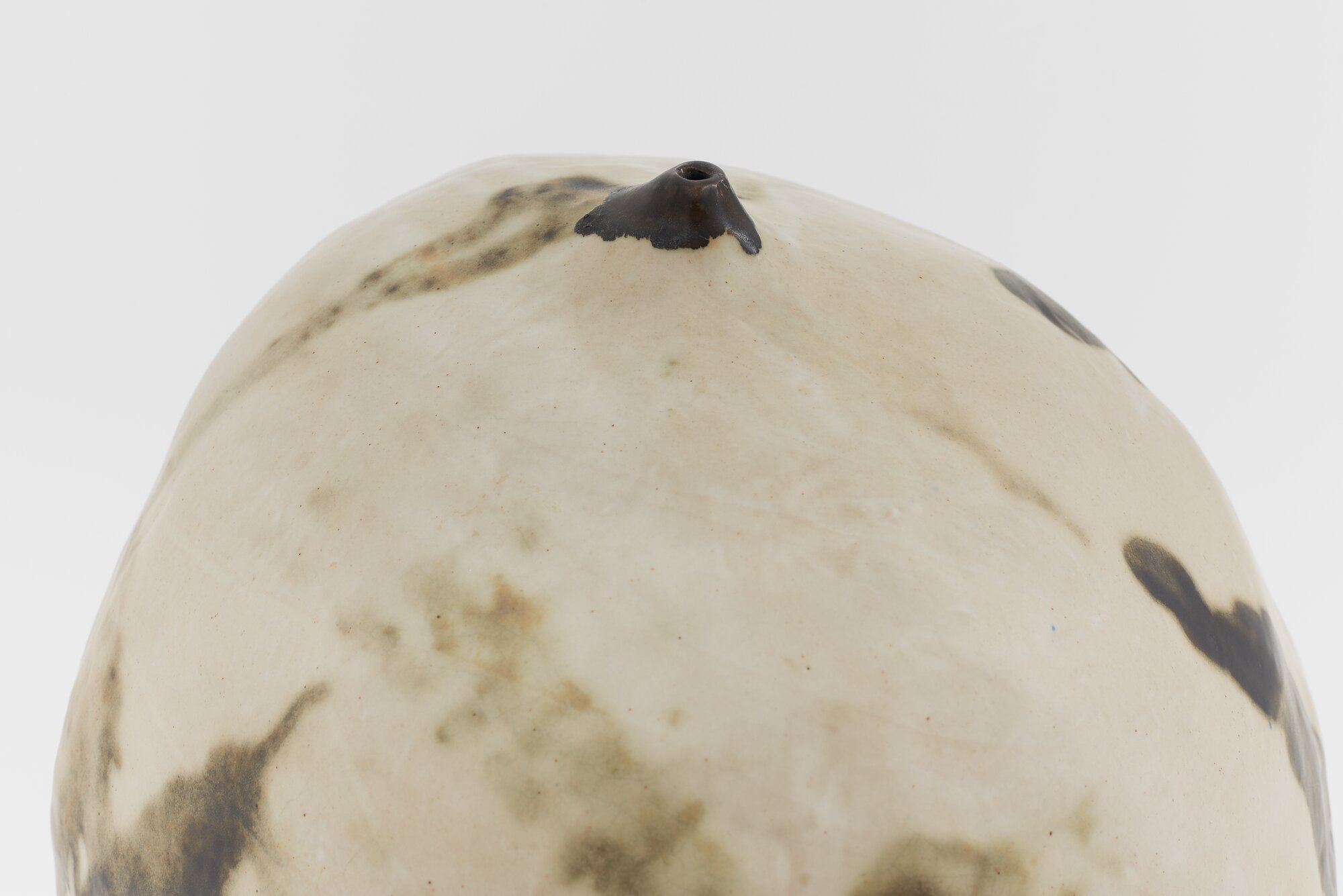 Detail of a round, beige ceramic vessel with a small, puckered opening at its top.