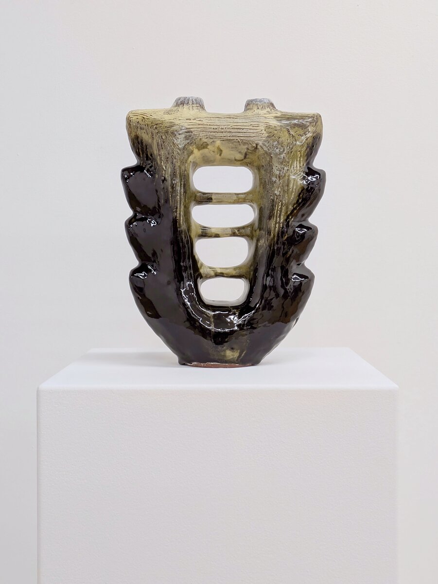 a large ceramic vessel with glossy black and yellow glaze sits on a white gallery plinth.