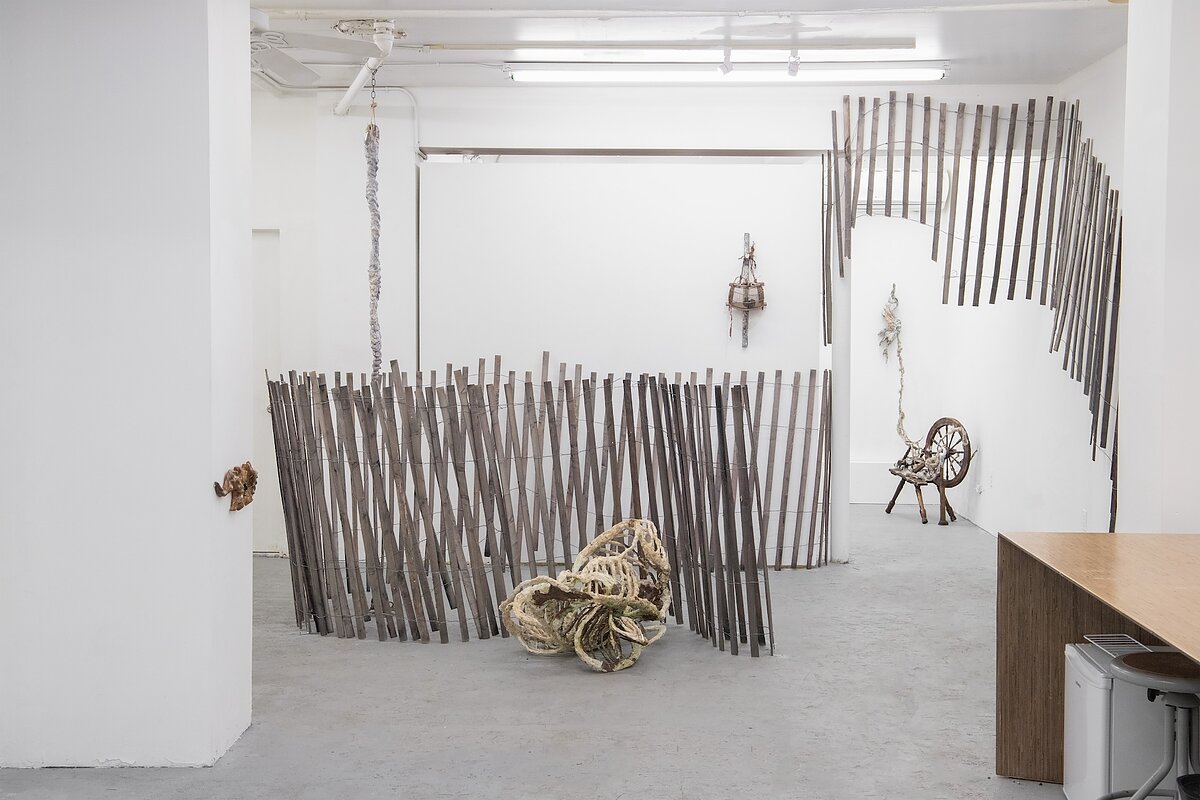 A gallery with white walls featuring a variety of sculptures that evoke fencing and bones. 