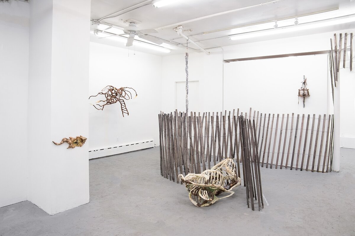 A gallery featuring a series of sculptures on the wall, hung from the ceiling, or assembled on the floor, resembling a wooden fence and bones. 
