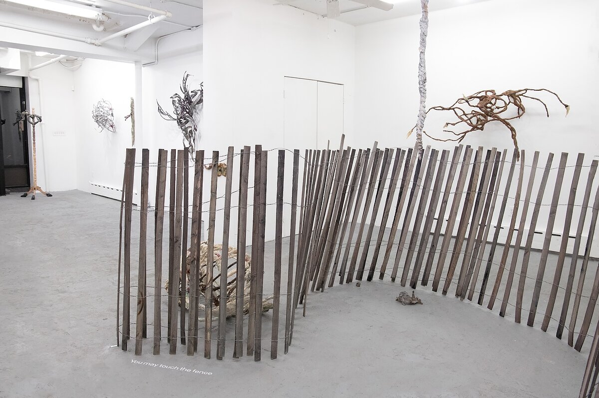 A gallery featuring a series of sculptures on the wall, hung from the ceiling, or assembled on the floor, resembling a wooden fence and bones. 