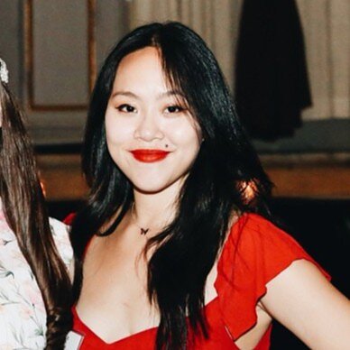 An Asian woman with long black hair, red lipstick, and red shortsleeved shirt 