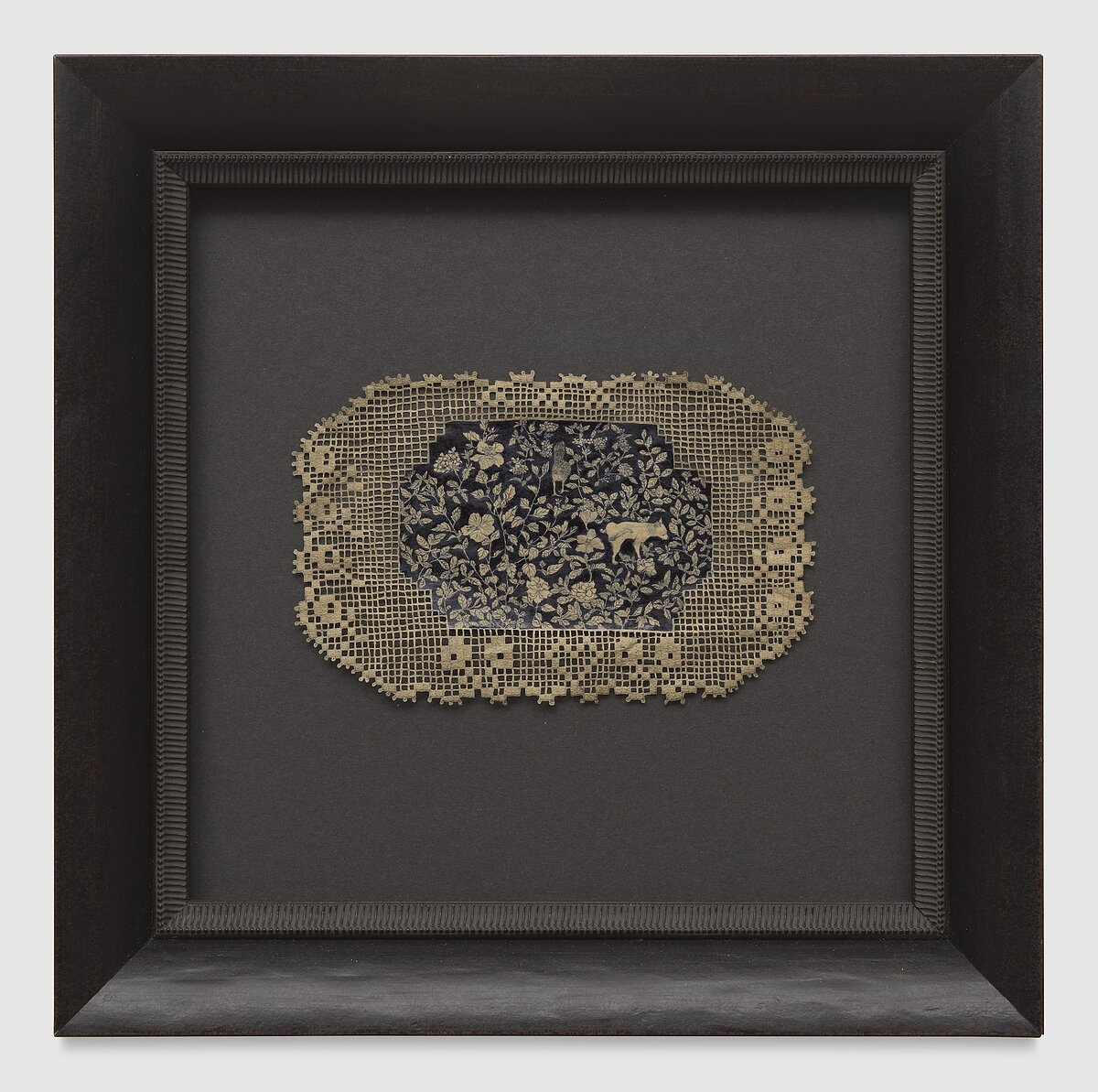A panel of lace with a blue-and-white floral illustration at its center, all meticulously carved out with an X-ACTO knife, hangs in a square black frame. 