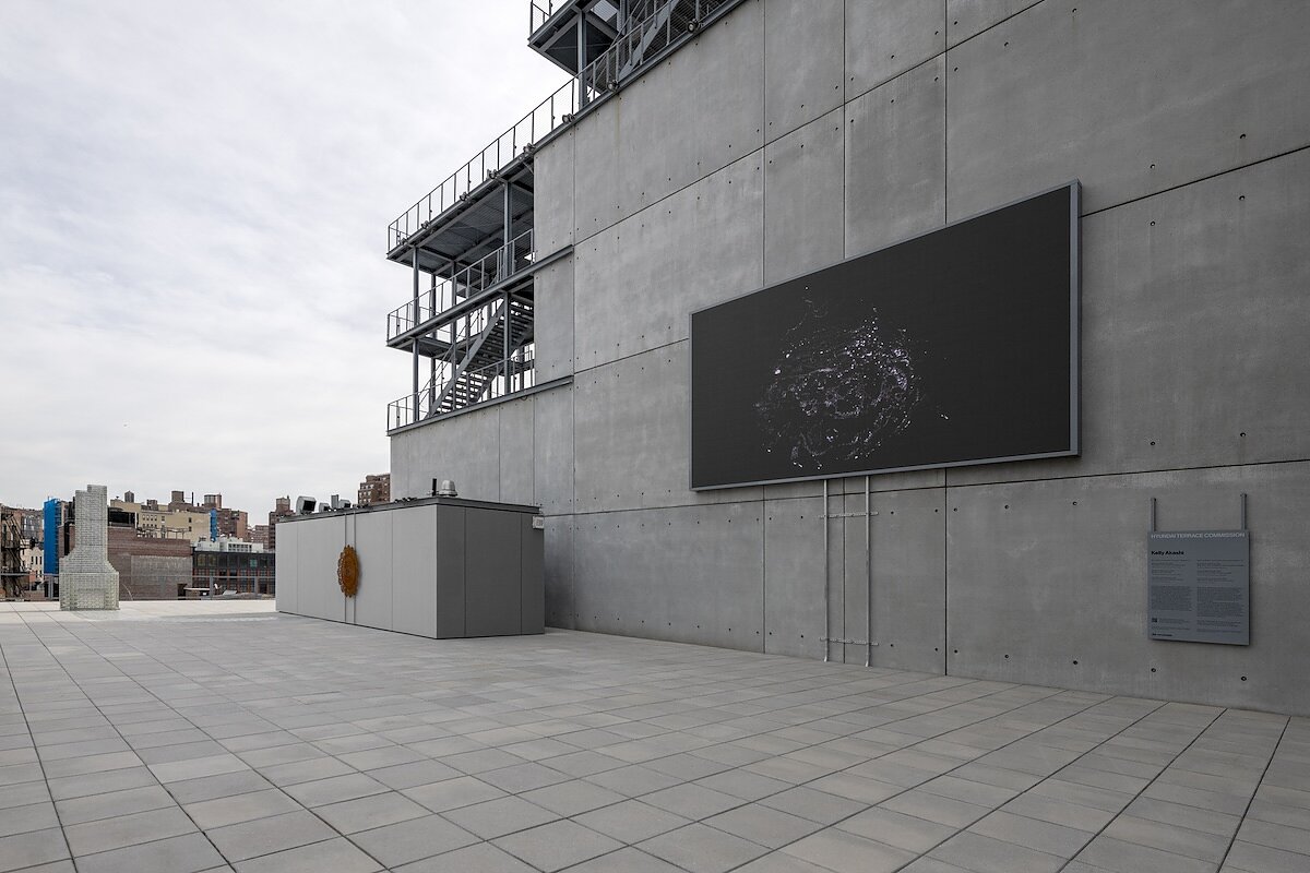 A grey NYC rooftop terrace features a giant LED screen playing an abstract work of art. 