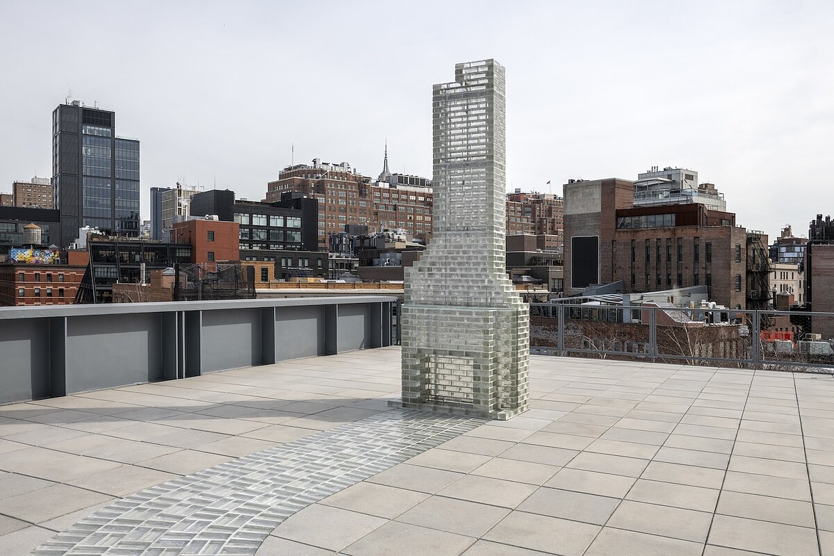 A sculpture made of glass bricks in the form of a fireplace with a brick road leading to its hearth on a NYC rooftop terrace.