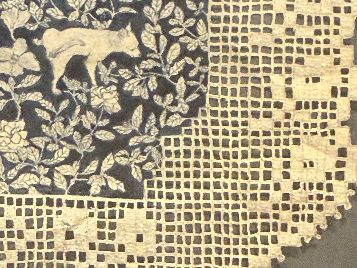 A panel of lace with a blue-and-white floral illustration at its center, all meticulously carved out with an X-ACTO knife, hangs in a square black frame. 