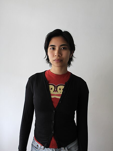 Asian American person with short cropped hair wearing a black cardigan and red T-shirt against a white background