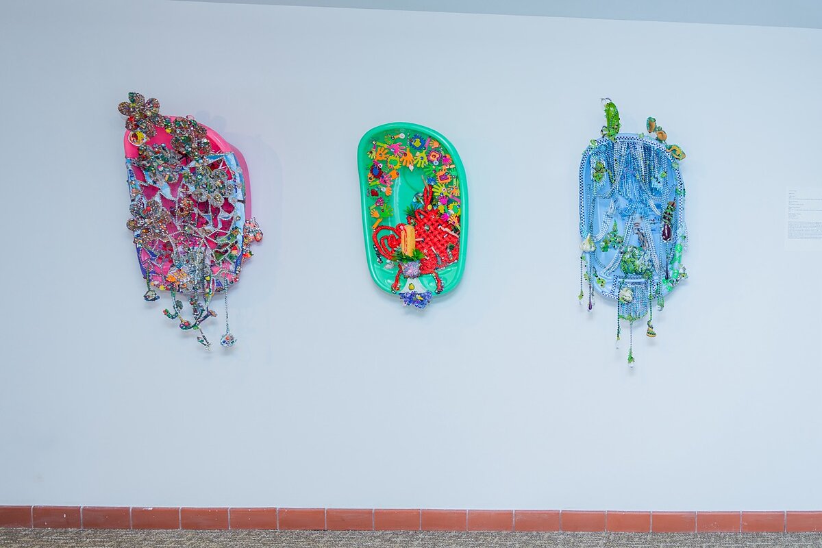 Three colorful sculptures in the shape of bathtubs hang from a gallery wall. 