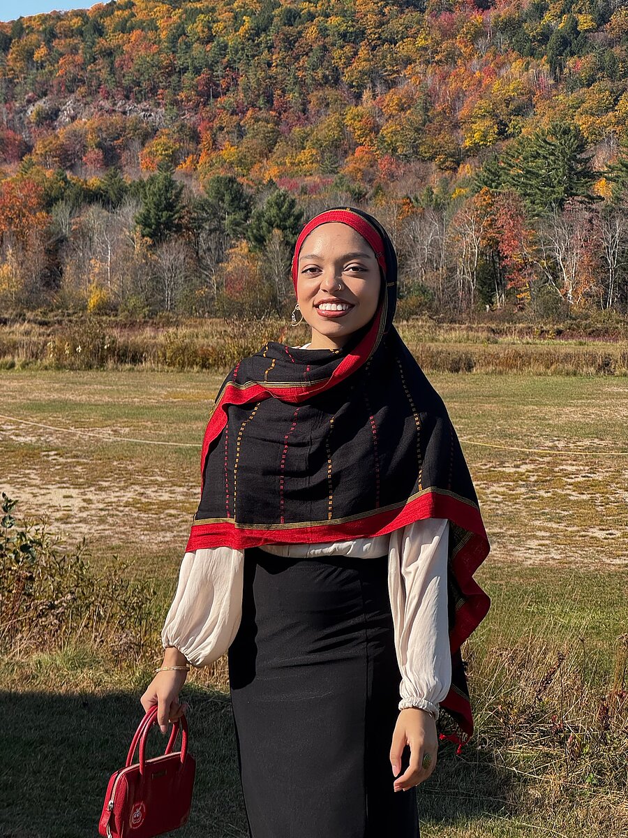 a woman wearing a black scarf with red border smiles against a forest background