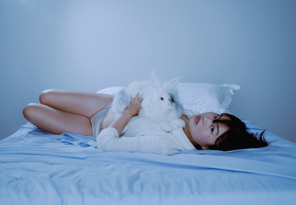 A woman lying on a bed holds a white rabbit.