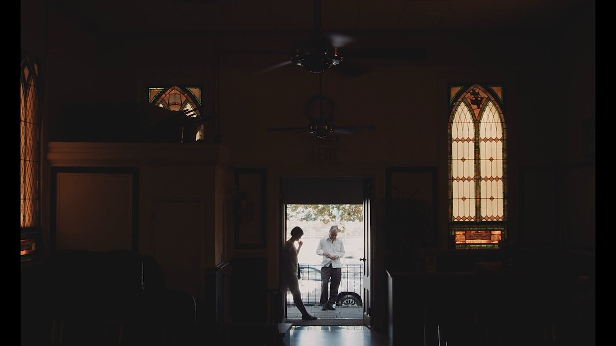 A man and woman stand in front of a church doorway.