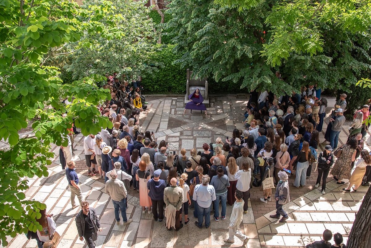 A crowd of people gather in a courtyard to watch a woman dancer perform. 