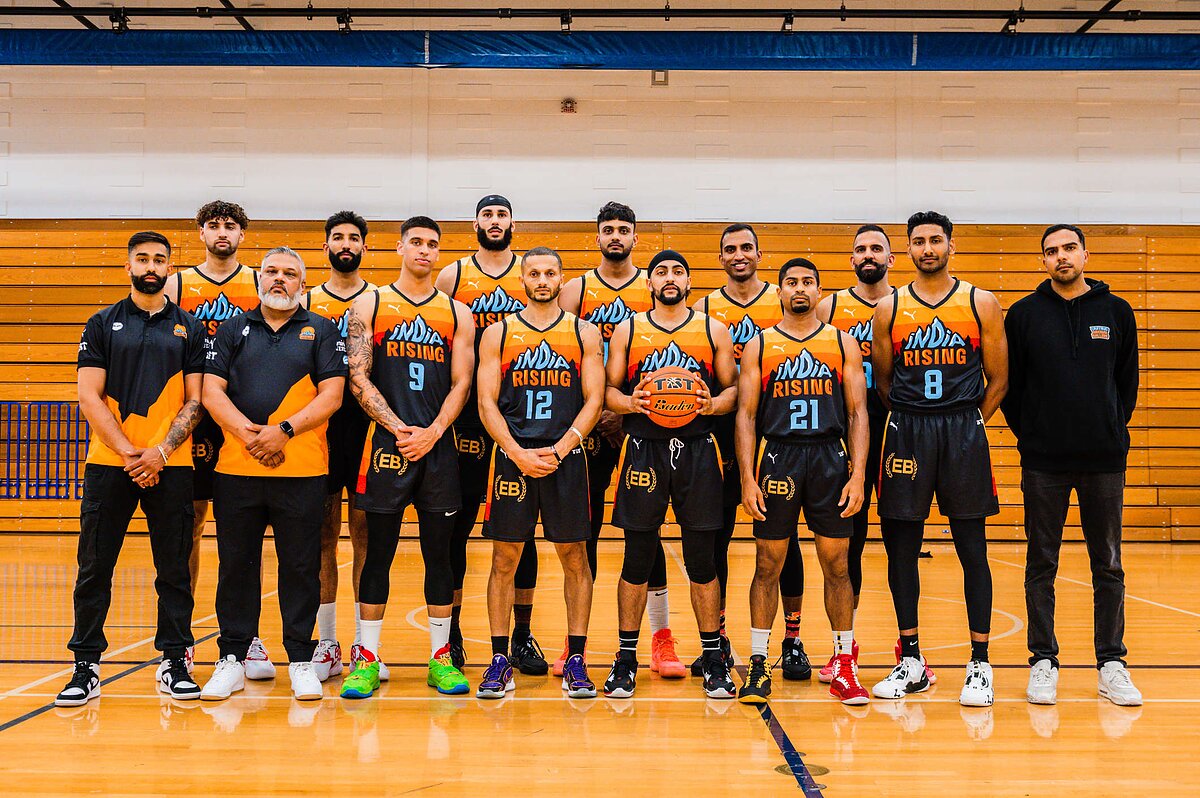 A team of basketball players in orange, black, and blue jerseys that say "India Rising" pose for the camera. 