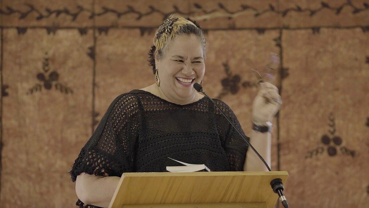 A woman with short cropped hair laughs at a podium. 