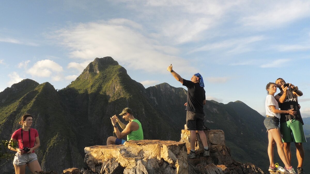 A group of tourists take photos in front of a mountain range.