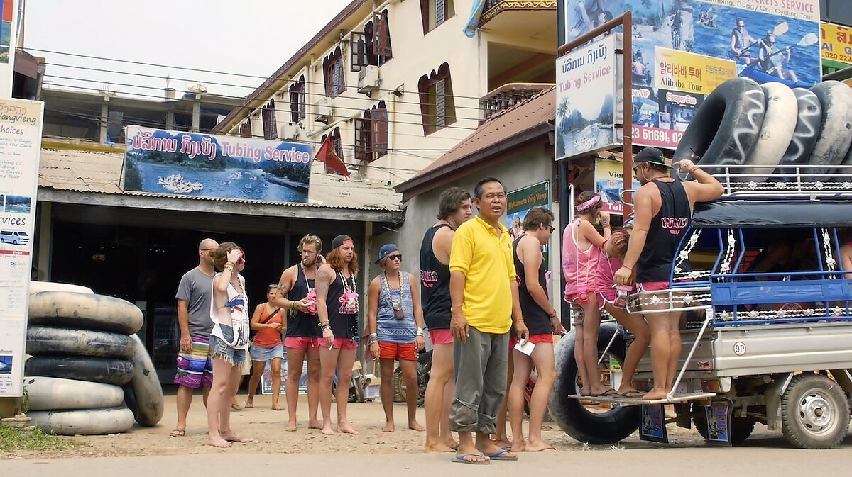 A crowd of people stand in line in front of a storefront for tubing.