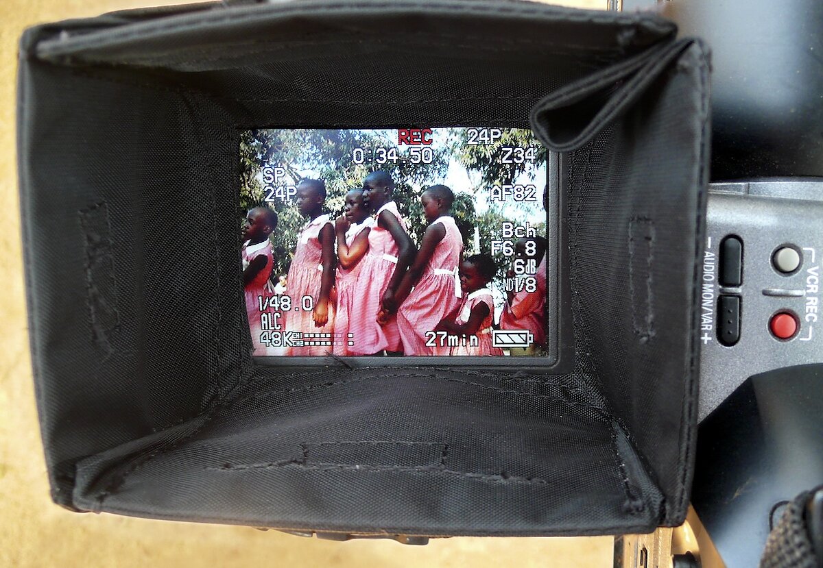 A scene of girls wearing matching pink dresses outside seen through a camera lens.