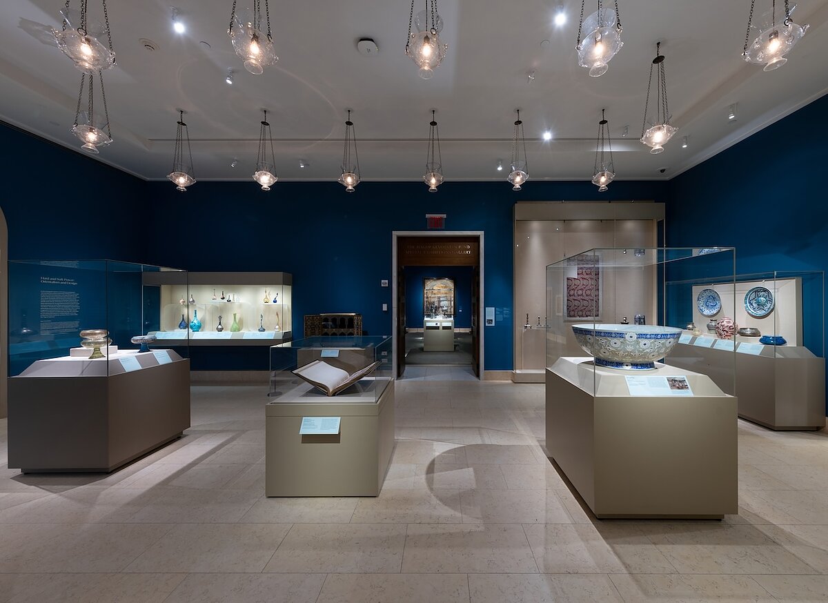 A gallery with blue walls filled with a variety of objects in glass vitrines.