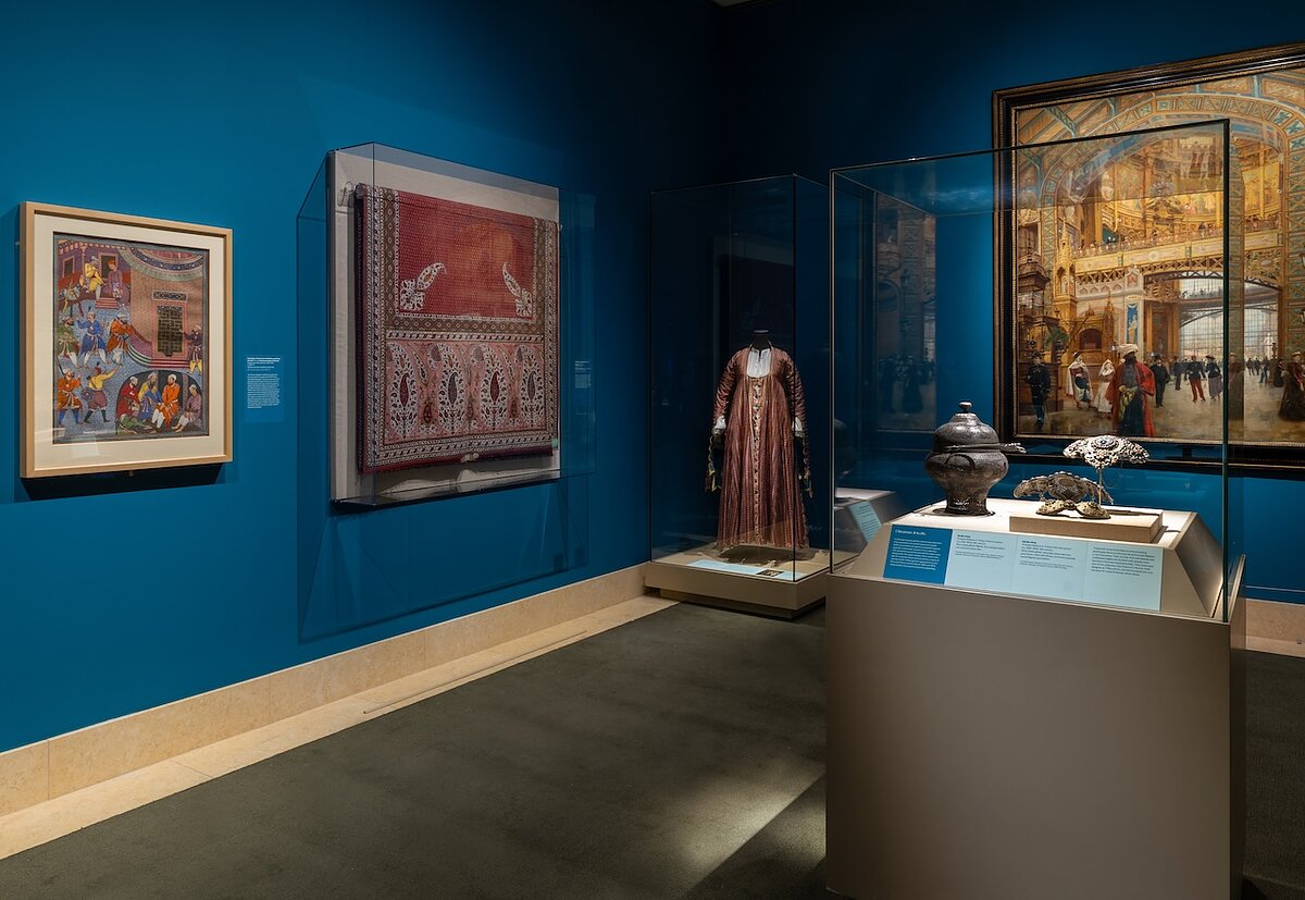 A gallery with blue walls filled with paintings and glass vitrines.