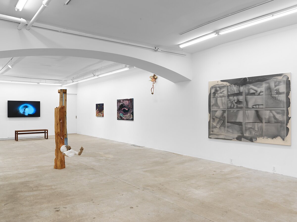 An installation shot of a gallery space featuring paintings, sculptures, and a video work. 