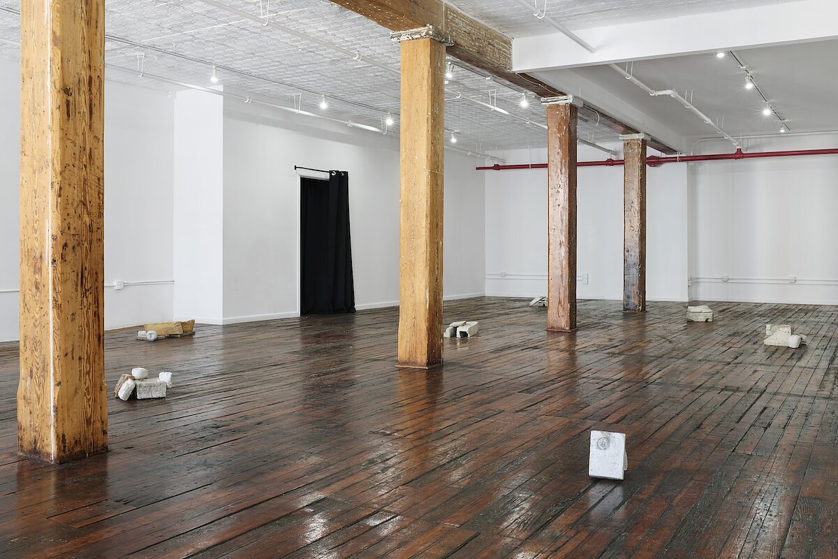 A gallery space with small concrete sculptures arranged on a wooden floor. 