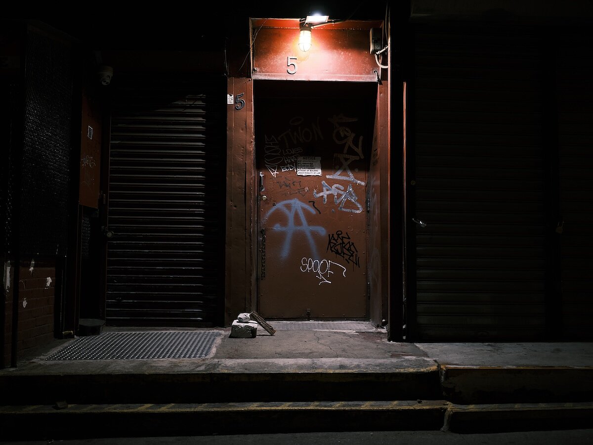 A city street and doorway with graffiti on it at night with a small arrangement of concrete shapes in front of it. 