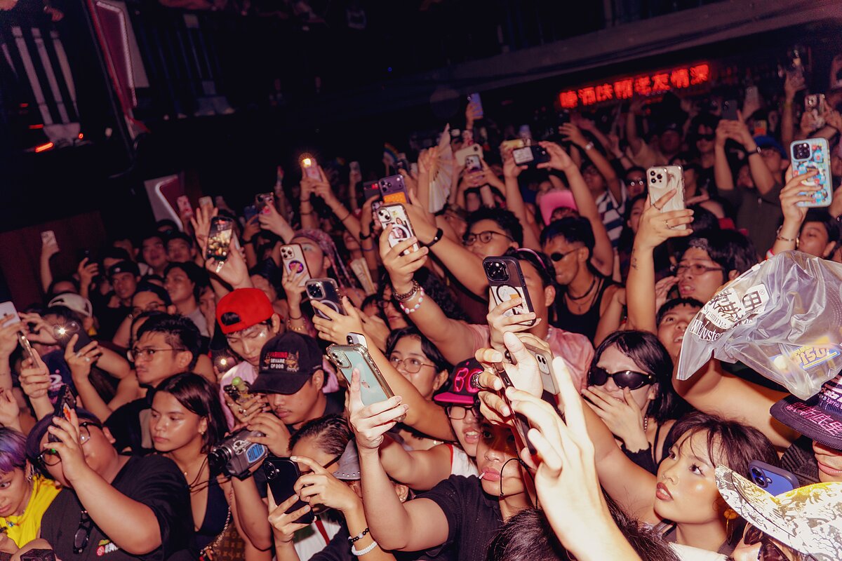 A crowd of people on a dance floor all facing the same direction and holding up smartphones to take video of something happening offscreen.